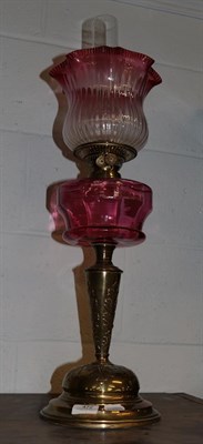 Lot 472 - A Victorian brass oil lamp with cranberry glass reservoir and shade