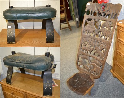 Lot 1354 - A pair of leather camel stool with ebonised and brass studded legs, together with an African tribal