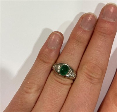 Lot 2040 - An Emerald and Diamond Ring, the cabochon emerald in a white collet setting, to shoulders inset...