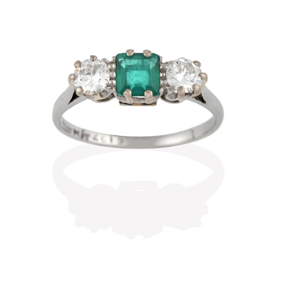 Lot 2043 - An Emerald and Diamond Three Stone Ring, the central step cut emerald flanked by round...