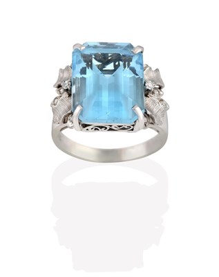 Lot 2101 - A Blue Topaz Ring, the emerald-cut blue topaz in a white four claw setting, to textured foliate...