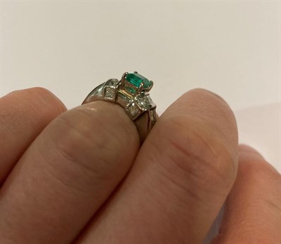 Lot 2116 - An Emerald and Diamond Ring, the emerald-cut emerald in a white four claw setting, flanked by a...