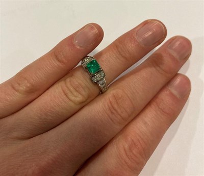 Lot 2116 - An Emerald and Diamond Ring, the emerald-cut emerald in a white four claw setting, flanked by a...