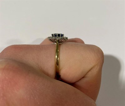 Lot 2153 - An 18 Carat Gold Sapphire and Diamond Cluster Ring, the oval cut sapphire within a border of...
