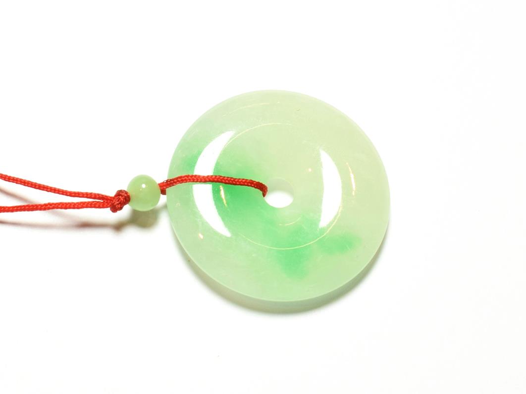 Lot 91 - A circular jade pendant, on a red cord necklace, pendant measures 3.7cm diameter