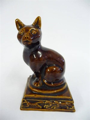 Lot 87 - A Treacle Glazed Terracotta Figure of a Seated Cat, 19th century, on a stepped rectangular base...