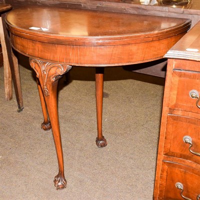 Lot 1134 - A reproduction crossbanded walnut demi-lune foldover card table, on scroll carved legs and ball and