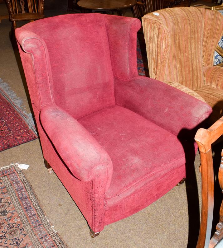 Lot 1144 - An early 20th century mahogany framed, deep seated, red upholstered wing back arm chair, moving...