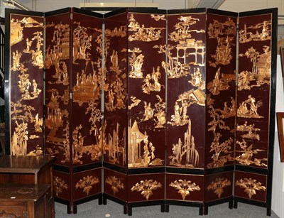 Lot 1241 - An imposing Chinese eight fold partition screen, decorated in relief with gilt figures and...