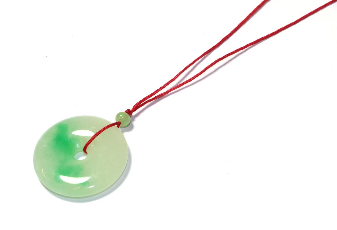 Lot 58 - A circular jade pendant, on a red cord necklace, pendant measures 3.7cm diameter