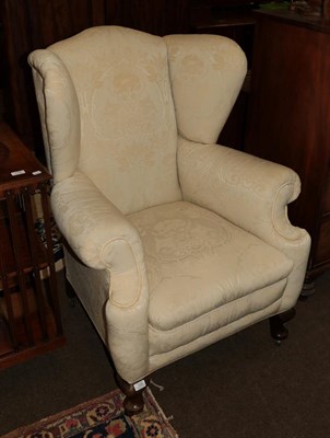 Lot 1299 - A Georgian style upholstered wingback armchair with scrolling arms and raised on cabriole feet