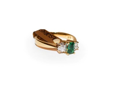 Lot 109 - An 18 carat gold emerald and diamond three stone ring, the step cut emerald flanked by round...