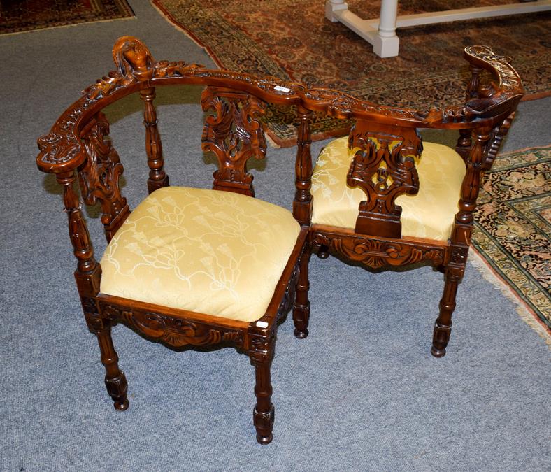 Lot 1066 - A reproduction carved mahogany conversation chair, with drop-in upholstered seats, ornamented...