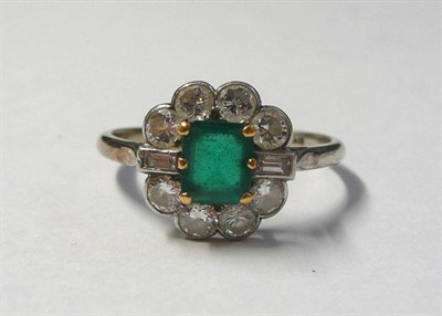 Lot 557 - A Mid 20th Century Emerald and Diamond Cluster Ring, the step cut emerald with truncated corners in