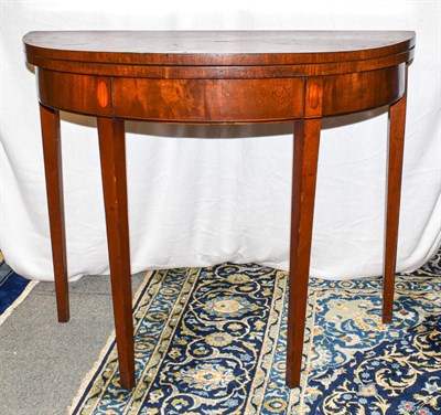 Lot 1216 - A George III crossbanded mahogany demi lune fold over card table, 90cm by 45cm by 74cm