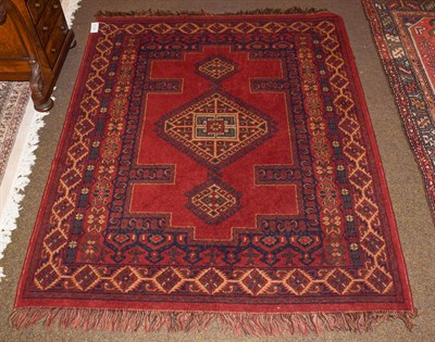 Lot 1155 - A machine made rug, the deep brick red field with hooked central gul, 168cm by 141cm
