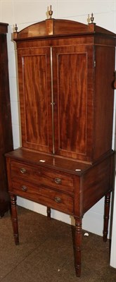 Lot 1311 - A Regency mahogany cabinet on two-drawer stand, with arched pediment having three brass finial with