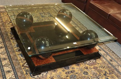 Lot 1379 - A modern glass top coffee table raised on four gloss black and burr wood spheres on a bevelled...