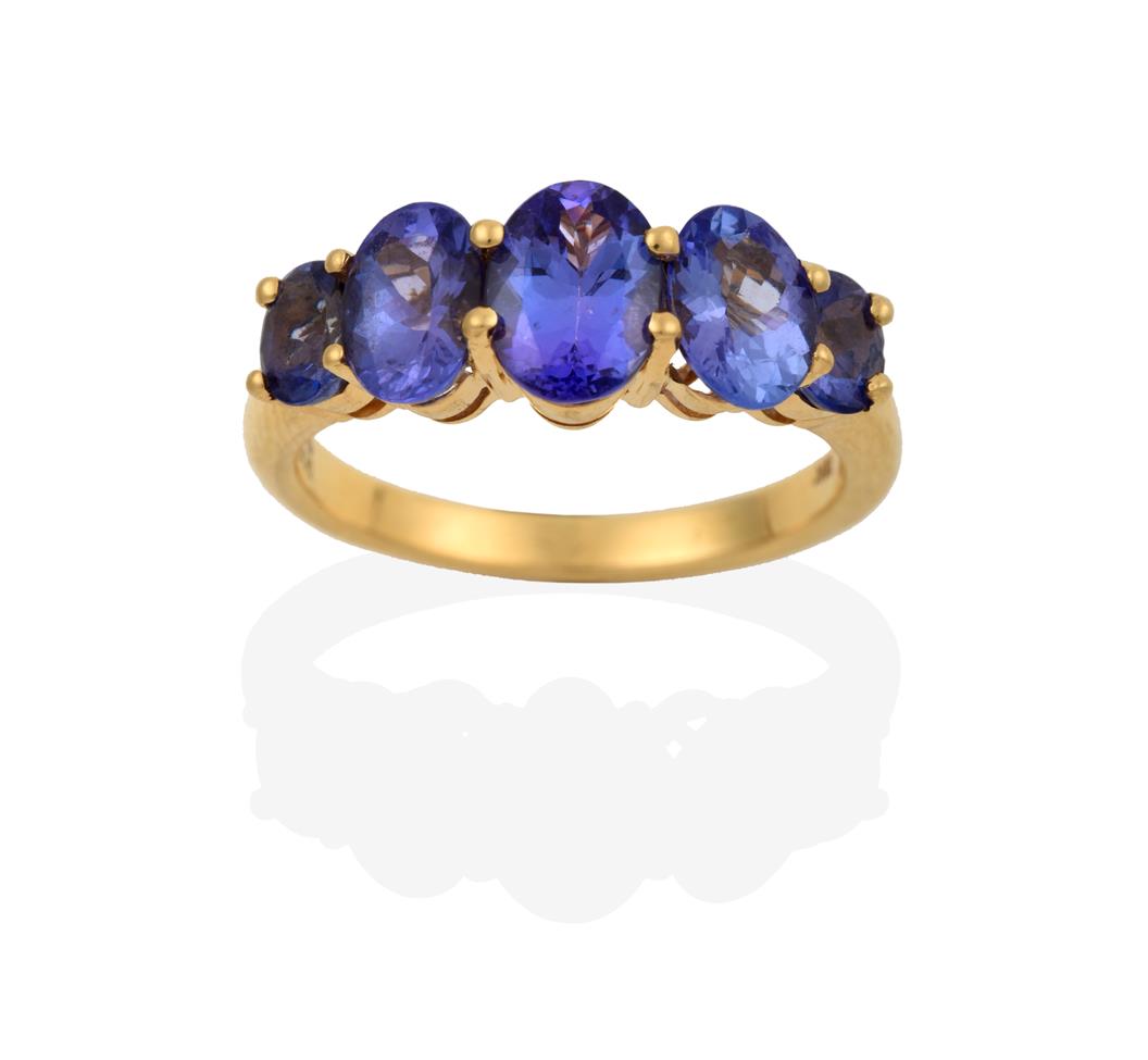Lot 2061 - An 18 Carat Gold Tanzanite Five Stone Ring, the graduated oval cut tanzanites in yellow claw...
