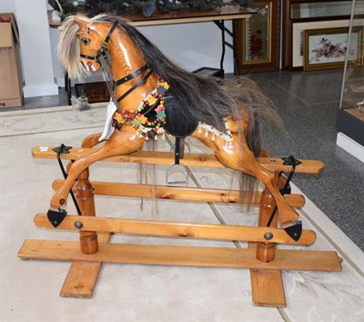 Lot 1223 - A carved wooden rocking horse with tack on a trestle base, 153cm by 115cm high