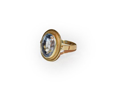 Lot 184 - A blue topaz ring, the oval cut blue topaz in a yellow rubbed over setting to a ropetwist...