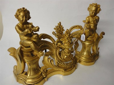 Lot 1319 - A Pair of French Gilt Brass Chenets, circa 1850, each worked with a seated cherub holding a nest of