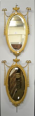 Lot 1127 - A pair of gilt framed oval mirrors in the manner of Robert Adam decorated with urns and ribbon tied