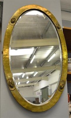Lot 1248 - An Arts & Crafts oval mirror with bevelled glass, in hammered brass mounted frame adorned with four