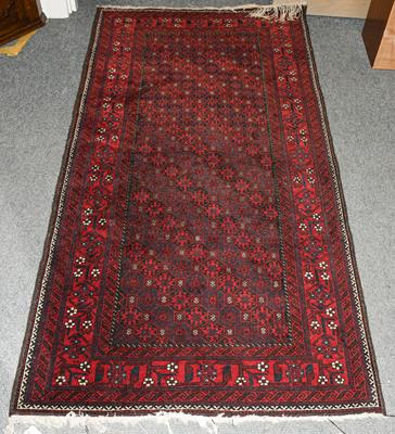 Lot 1218 - A Baluch rug the honeycomb lattice field of hooked guls enclosed by a border of angular vines,...