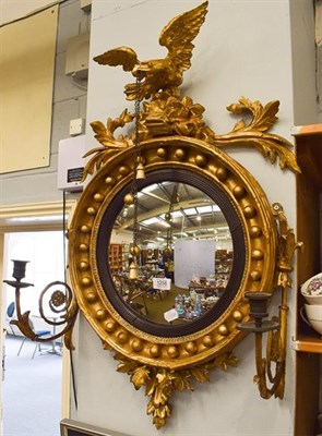 Lot 1258 - A Regency convex wall mirror surmounted with eagle, chain and tassles, with candle sconces, the...
