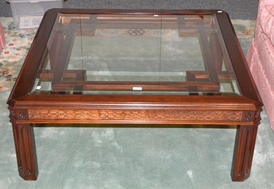 Lot 1268 - A reproduction mahogany glass topped coffee table with blind fret carving, raised on panel...