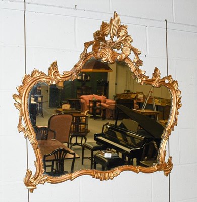 Lot 1337 - A 20th century giltwood wall mirror, with floral pediment and adorned with stylised leaf...