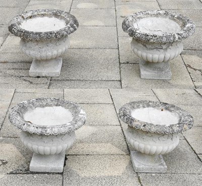 Lot 1344 - A set of four weathered composition garden urns with egg and dart borders and part gadrooned...