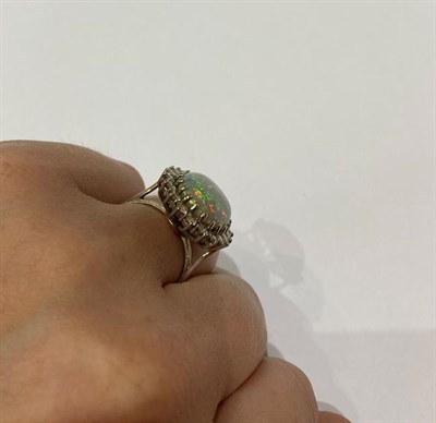 Lot 2249 - An 18 Carat White Gold Opal and Diamond Cluster Ring, the oval cabochon opal within a border of...