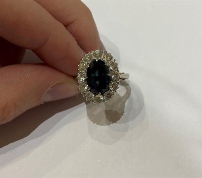 Lot 2277 - A Sapphire and Diamond Cluster Ring, the oval cut sapphire within a border of round brilliant...