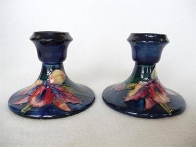 Lot 1729 - A Pair of Walter Moorcroft Orchid Pattern Squat Candlesticks, circa 1950, on a blue ground,...