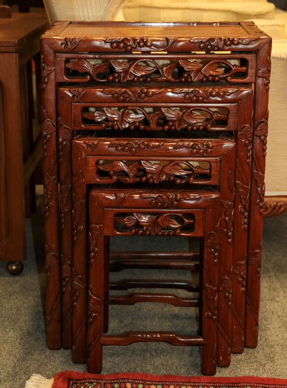 Lot 1093 - A 20th century Chinese hardwood nest of four tables carved with leaves and berries, 47cm by 34cm by