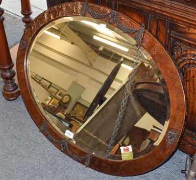 Lot 1265 - An early 20th century planished copper oval wall mirror, with goat head and swag relief detail,...