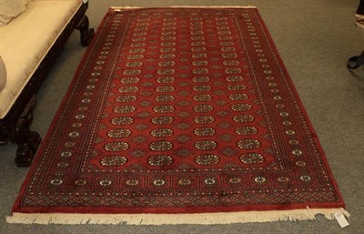 Lot 1077 - Paskistani Bukhara rug, the deep terracotta field with four columns of guls enclosed by stellar...