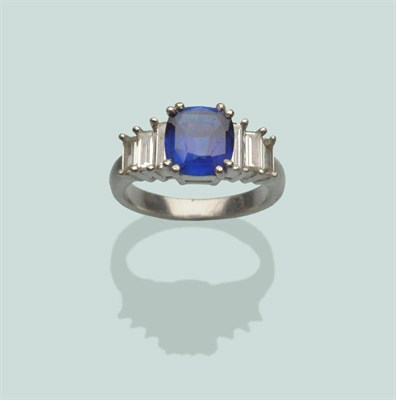 Lot 663 - A Sapphire and Diamond Ring, a cushion cut sapphire in white double claw settings, between trios of