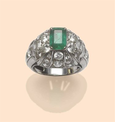 Lot 513 - An Emerald and Diamond Bombé Style Ring, a step cut emerald in a white four claw setting, over...