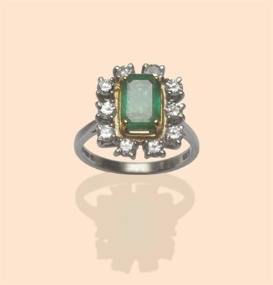 Lot 514 - An 18 Carat Gold Emerald and Diamond Cluster Ring, the step cut emerald in a yellow corner claw...