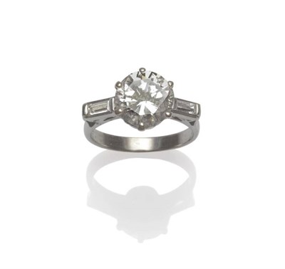 Lot 530 - A Diamond Solitaire Ring, a round brilliant cut diamond with a baguette cut diamond to each...