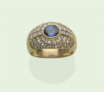 Lot 605 - A Sapphire and Diamond Cluster Ring, an oval mixed cut sapphire in a yellow collet setting with...