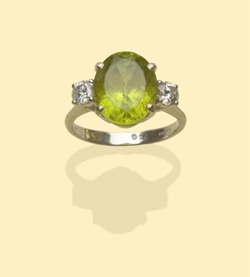 Lot 641 - An 18 Carat White Gold Peridot and Diamond Three Stone Ring, the oval cut peridot flanked by a...