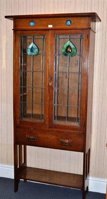 Lot 1282 - An Arts & Crafts Oak Glazed Bookcase, the overhanging top above a frieze mounted with two...