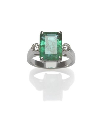 Lot 469 - An Emerald and Diamond Three Stone Ring, the emerald-cut emerald in a white four claw setting, with