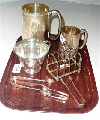 Lot 405 - A silver mug, christening mug and teacup, three silver sugar tongs and a plated toast rack