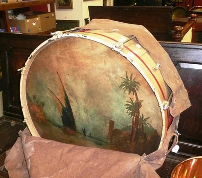 Lot 1643 - A bass drum, the skin painted with a Arab river landscape with cream and red painted wooden...