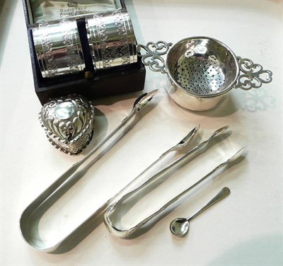 Lot 239 - A cased pair of silver napkin rings, a silver strainer, two pairs of tongs and a trinket box